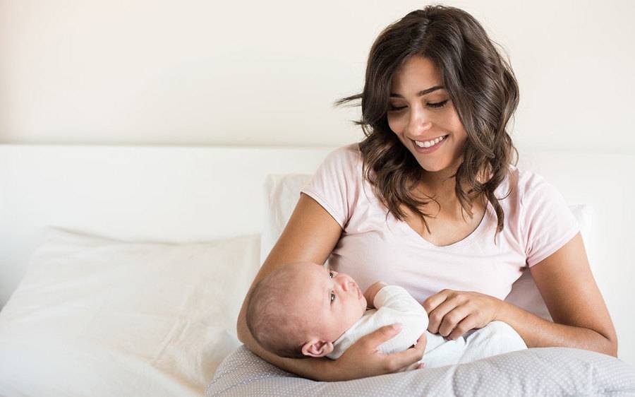 A young mother cradles her infant and smiles as she welcomes the new baby into her home.