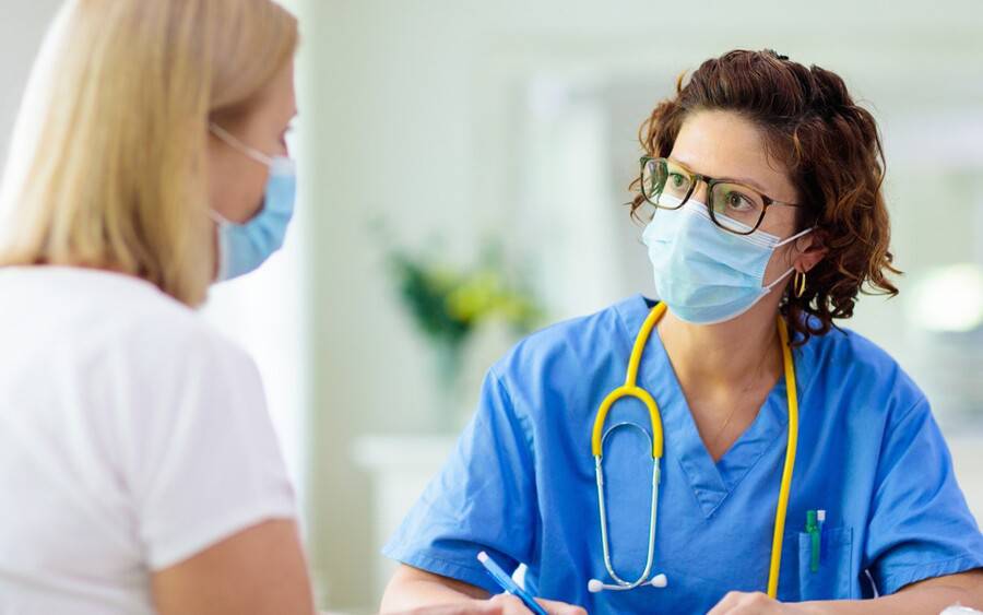 A nurse wearing a mask talks with a patient wearing a face covering.