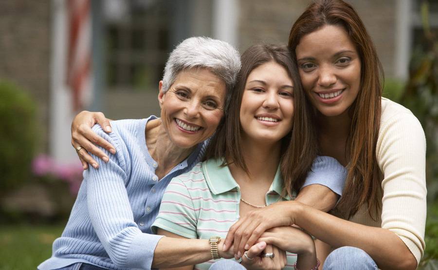 Multi-generational family of women smiling outside their family home, representing different stages of life and OB-GYN services.