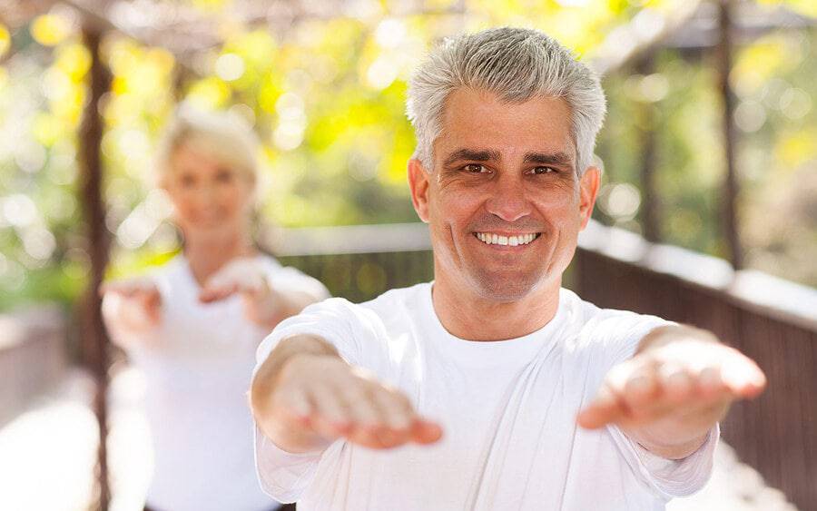 A mature couple exercising outside, working on balance, illustrating how they are working on balance as a way to prevent falls.