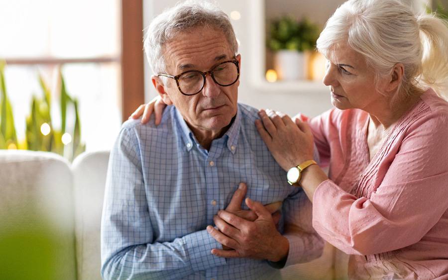 Older man grabbing his chest in pain with his wife coming to his aid.