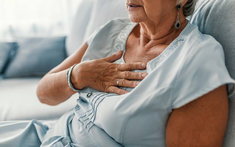 An older woman with heart failure clutches her chest in pain.