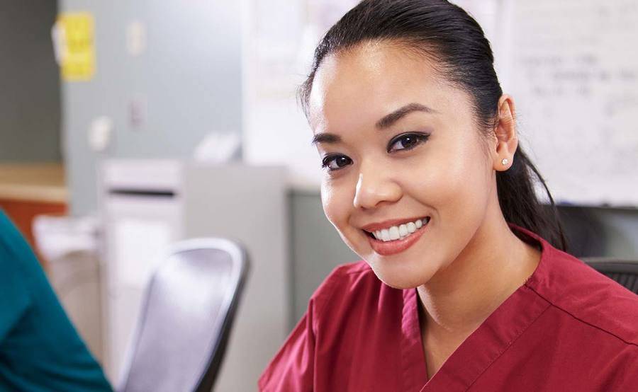 A smiling, young Asian nurse at a desk represents the personalized cancer support you get from the oncology nurse navigators at Scripps.