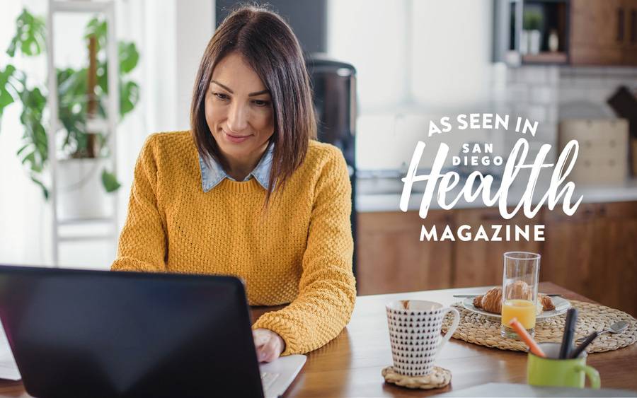 A woman is concentrated on her laptop while reviewing Scripps guide for open enrollment in order to help her decide the best health plan for her and her family.