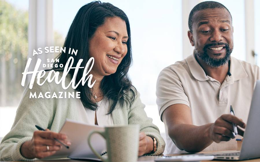 A man and a woman smile as they compare health insurance plans in preparation for open enrollment. - San Diego Health Magazine