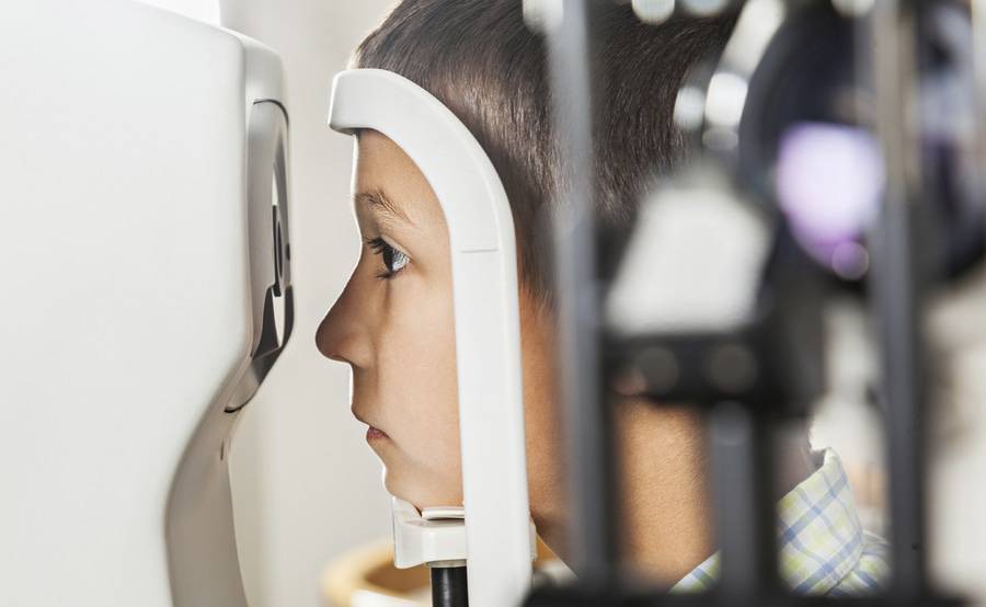 A boy looks into a machine as part of an eye exam, representing one of the many pediatric eye care capabilities