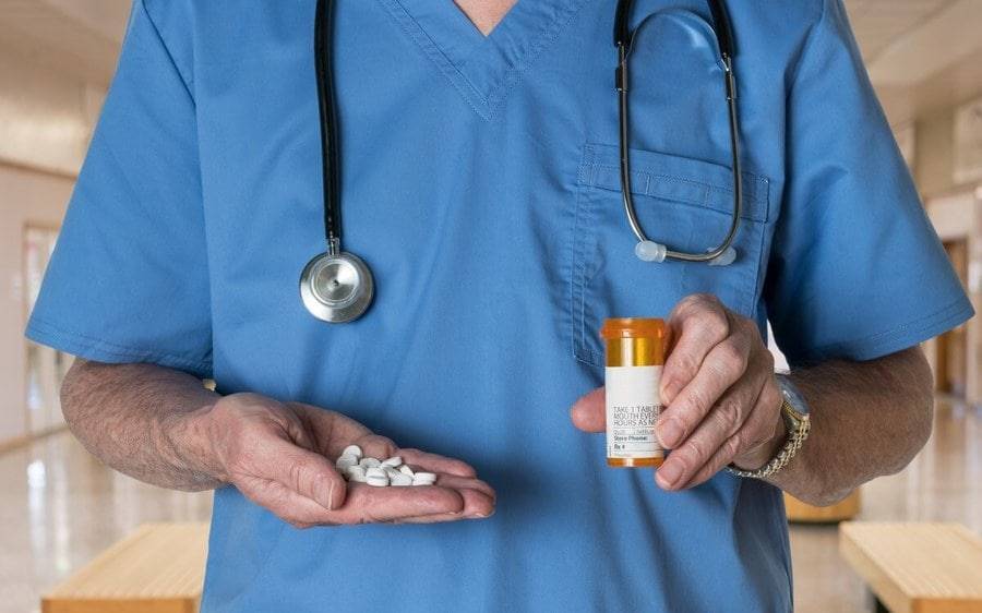 A doctor stands in a hospital hallway with a handful of prescribed opioids and the prescription bottle..