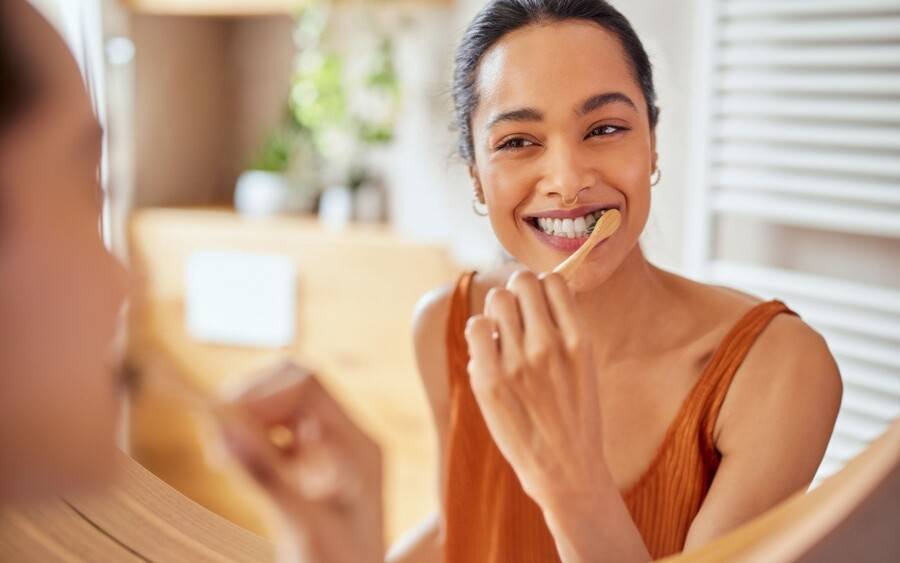 Oral hygiene; woman brushing teeth in front of mirror.