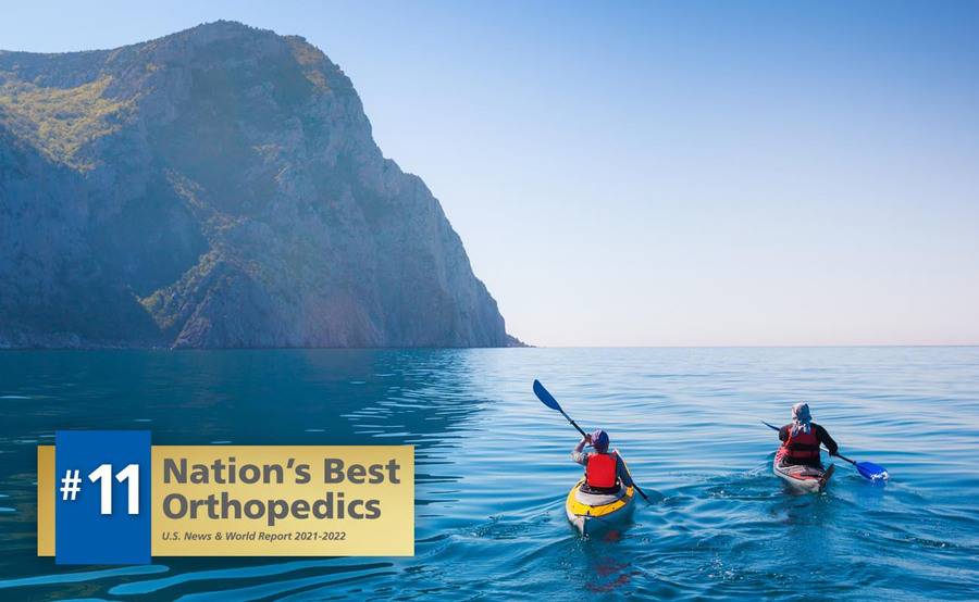 Two people paddle their kayaks around a mountain, representing an actively lifestyle after shoulder surgery.