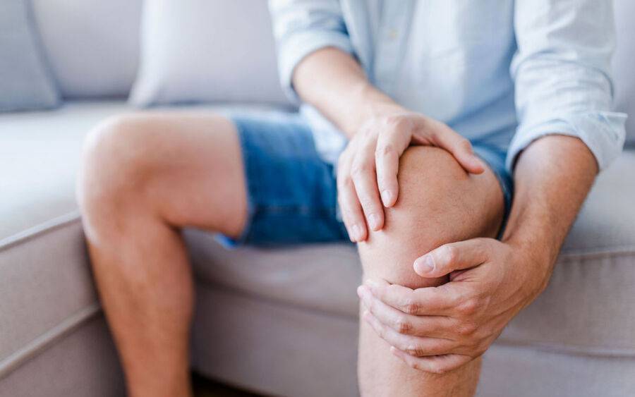 A man holds his knee in pain, suffering from osteoarthritis.