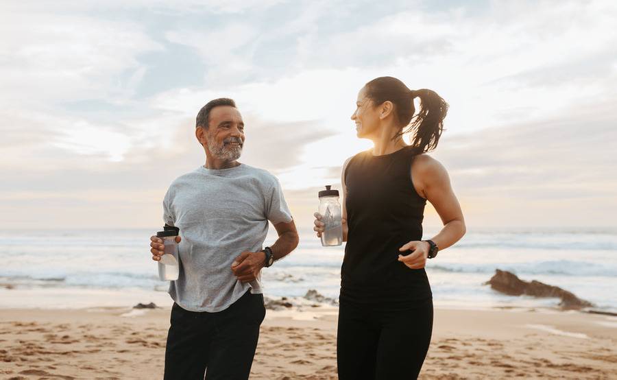 An older man and woman exercise at the beach representing a quicker recovery from outpatient surgery.