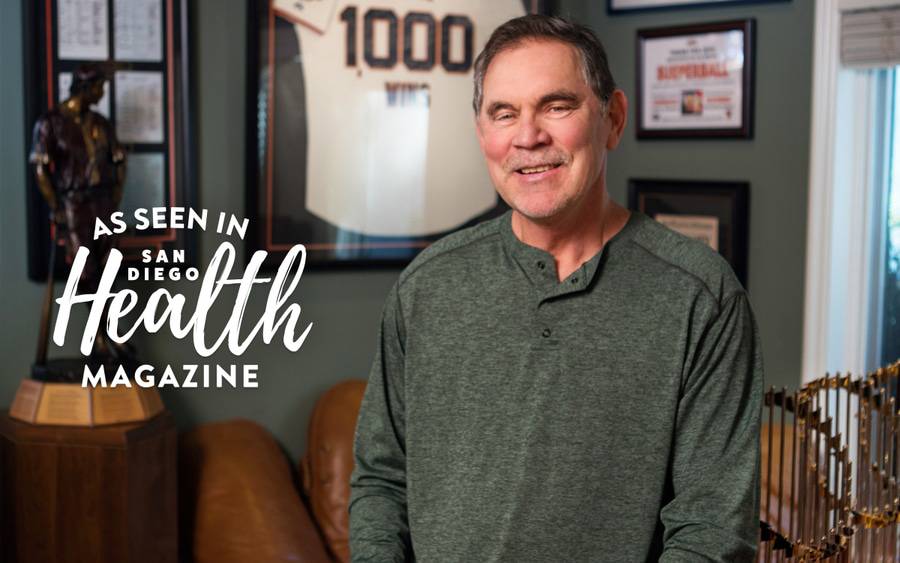 Bruce Bochy, former San Diego Padres manager, smiles and sits infront of memorabilia, grateful to be free from atrial fibrillation after treatment at Scripps.