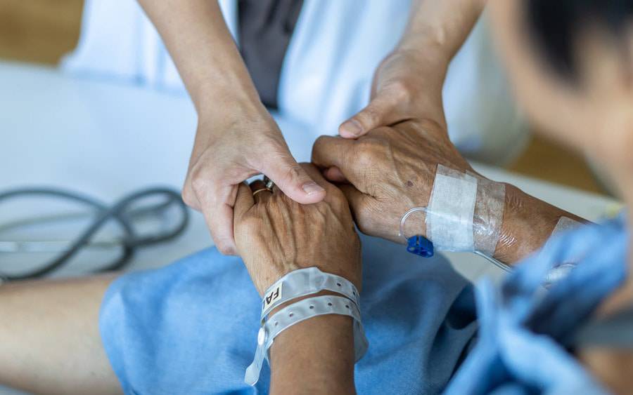 A caregiver holds the holds the hands of a palliative care patient.