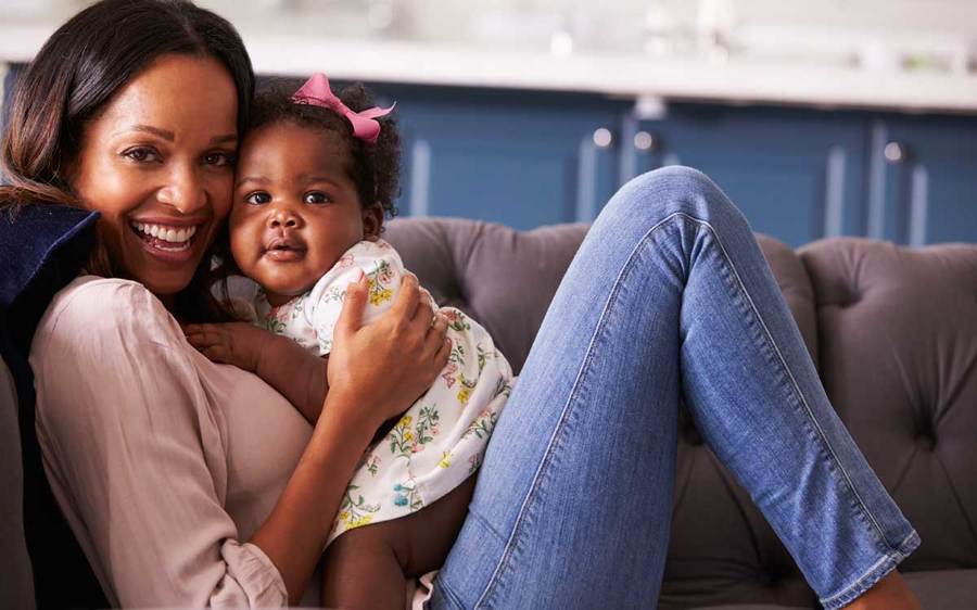 A happy mother and baby rest on the couch together