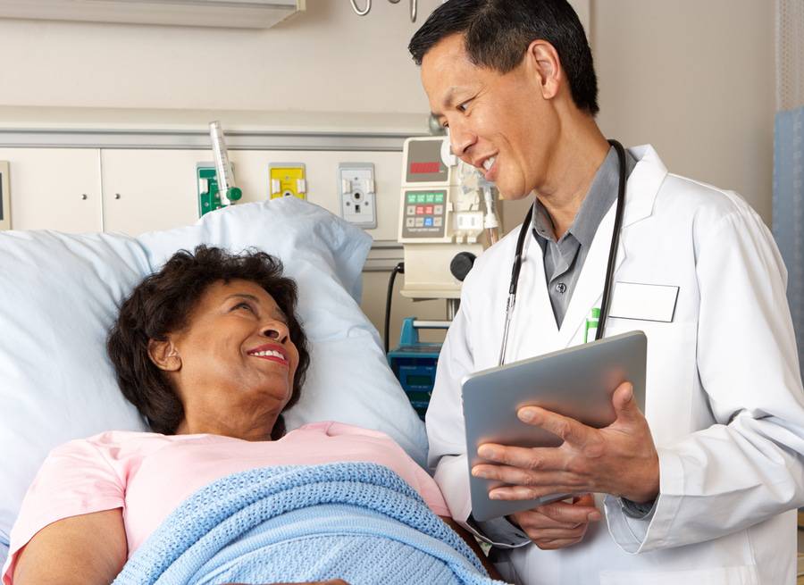 A doctor discusses health issues with a smiling patient in hospital bed.