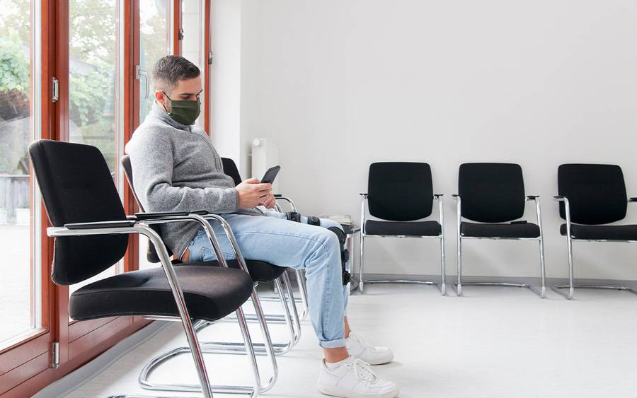 A patient waits to be called in waiting room, wearing mask to protect his health.