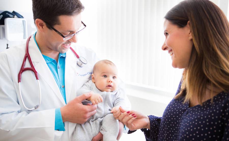 Dr. Daniel Lichtmann, Pediatrician at Scripps Clinic holding an infant patient with the mother smiling.