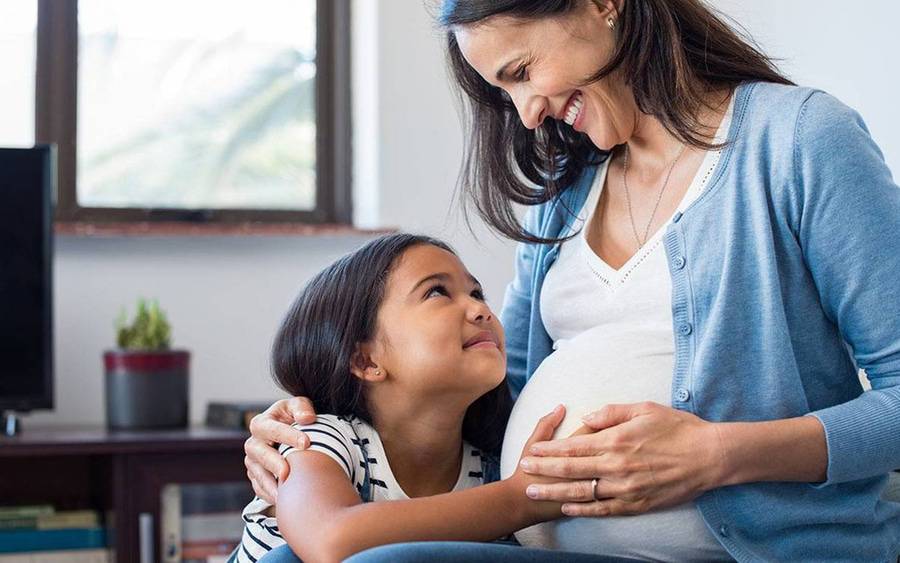 A mother to be and her young daughter holding pregnant stomach, representing healthy and happy mom to be. 