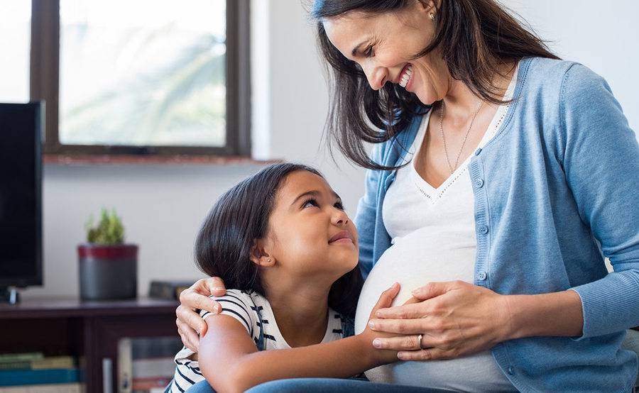 A pregnant woman embracing her child and smiling at her.