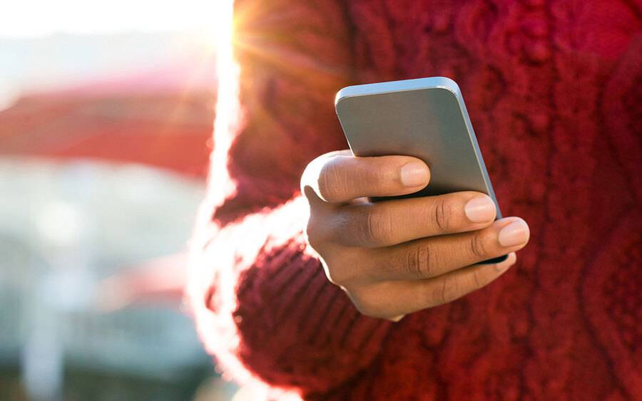 A person outside while the sun is shinning and holding their smartphone.