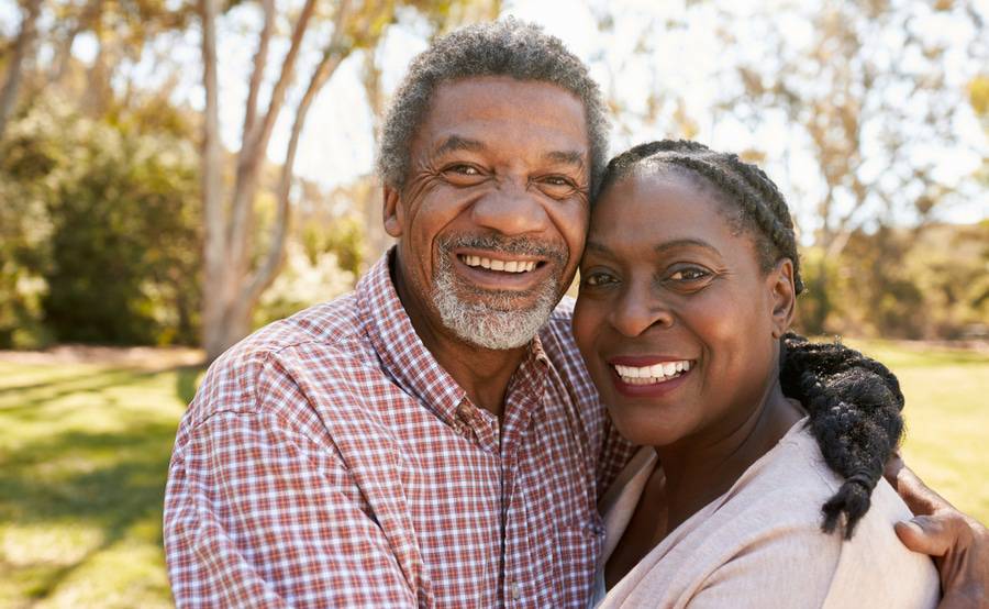 A smiling mature couple hugs in a park, representing the variety of people who need a PET scan.