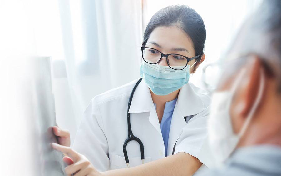 A physician talks to a senior patient about X-ray results. Both people are wearing masks during the COVID-19 pandemic. 