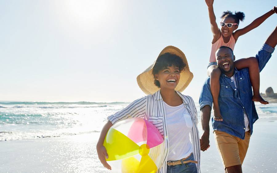 A young black family joyfully plays at the beach, knowing their summer health is supported by Scripps virtual care.