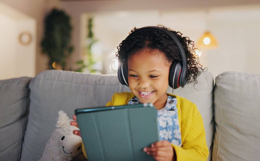 A child laughs while engaging with an educational online program on her tablet.