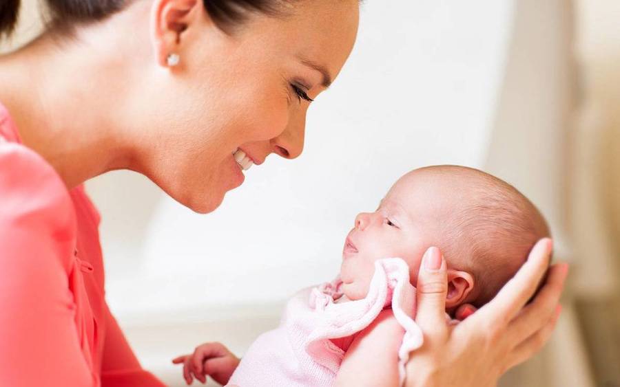 A mother smiles while holding and looking at her baby.