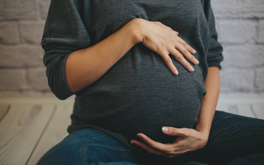 A pregnant woman holds her belly. Article focus is banking baby's cord blood.