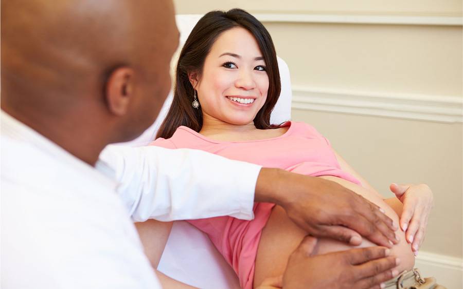 A pregnant woman smiles while being examined by her obstetrician.
