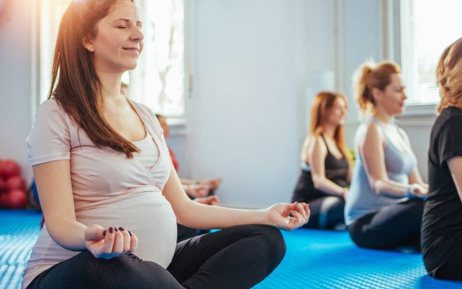 A pregnant woman closes her eyes in a relaxing pose during a prenatal yoga class.