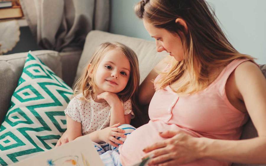A pregnant mother shares a caring moment with her daughter in a pleasant indoor setting.