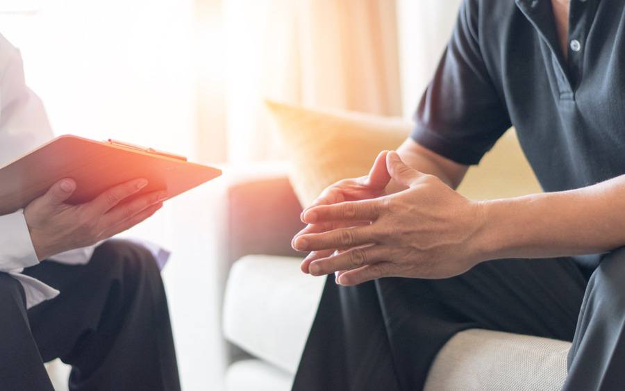 A man touches his fingertips together while talking with a psychologist.