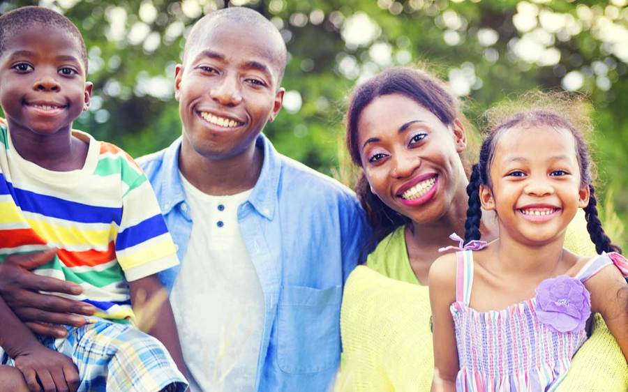 A smiling family of four relaxes in a pleasant outdoor park setting.