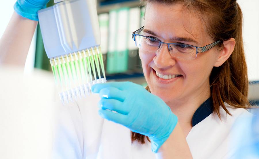A smiling scientist loads samples with an automatic multichannel pipette, representing the many types of research conducted at Scripps Health.