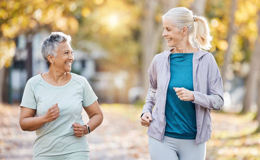 Two senior women smile as they walk outdoors representing successful rheumatology treatments. 