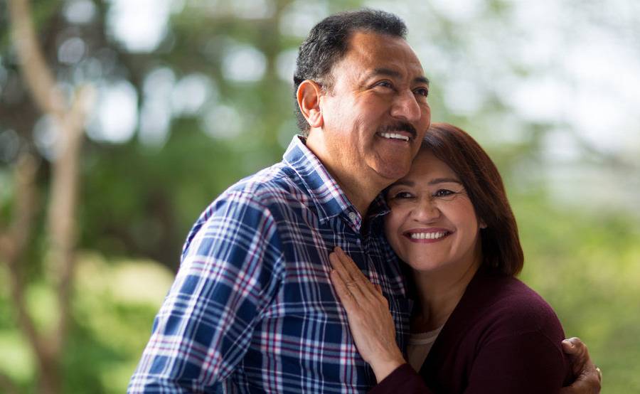A couple smiles while sharing a hug outdoors.