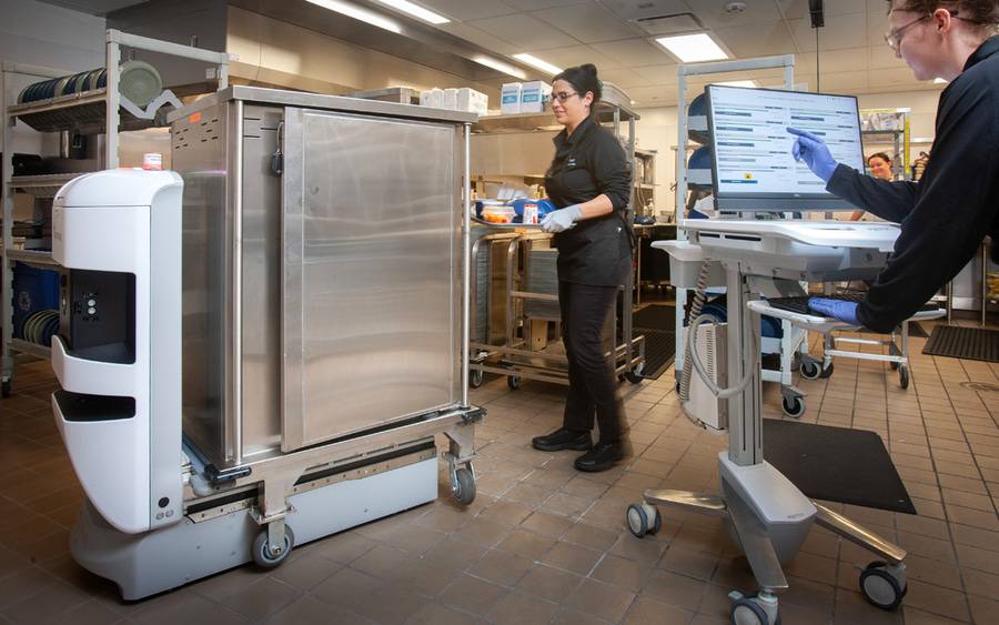 A staff member checks settings on a robotic cart that helps deliver patient food in the hospital.