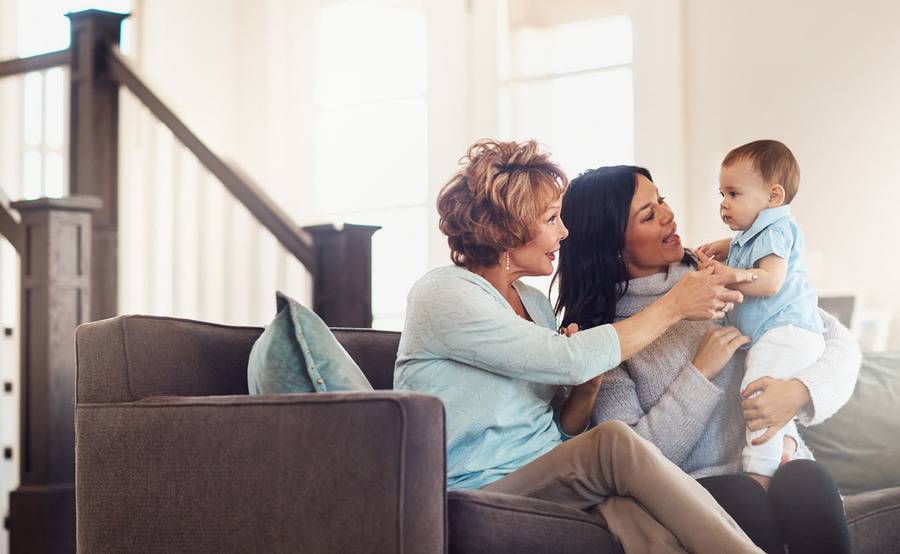 Two women sit together on a couch while one of them holds a baby, representing cross-generational gynecologic care at Scripps.