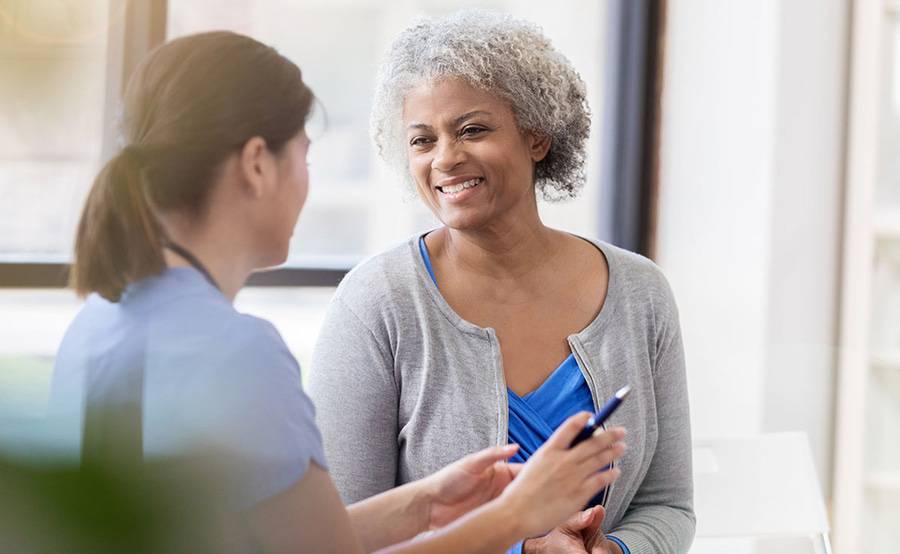 A woman smiles while talking to a surgeon in a sunlit room, representing modern robot-assisted gynecologic surgery at Scripps.