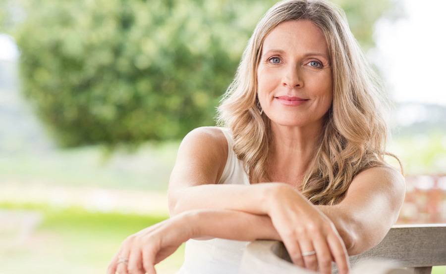 A woman smiles while sitting with her arms folded in front of her on a sunny day.