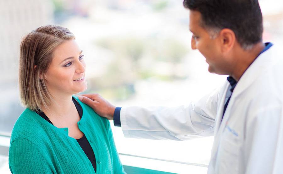 A woman smiles while talking to a surgeon in a sunlit room, representing modern robot-assisted gynecologic surgery at Scripps.