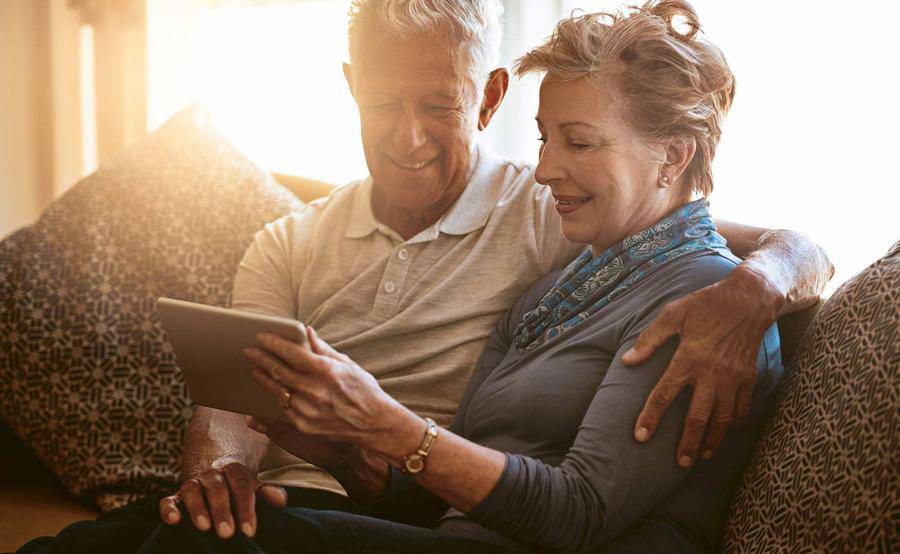 A couple sits together on a couch while looking at a tablet device.