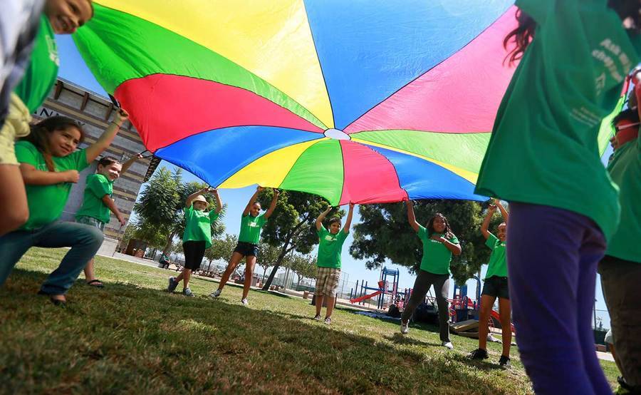 Children play with a large, colorful parachute in a park, representing the impact of our community health programs.