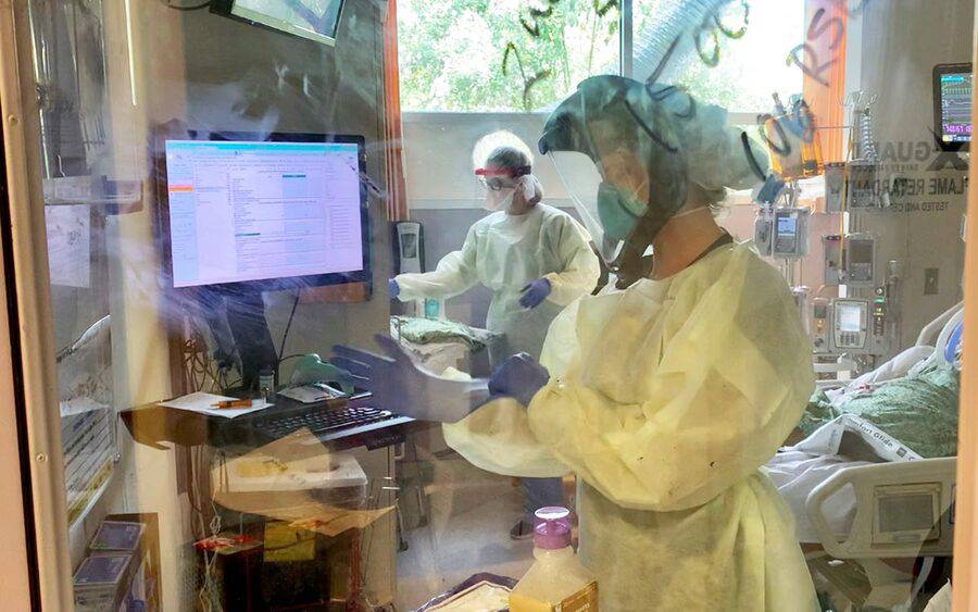 A Scripps medical professional adjusts their gloves and PPE while inside a COVID patient's ICU room. 