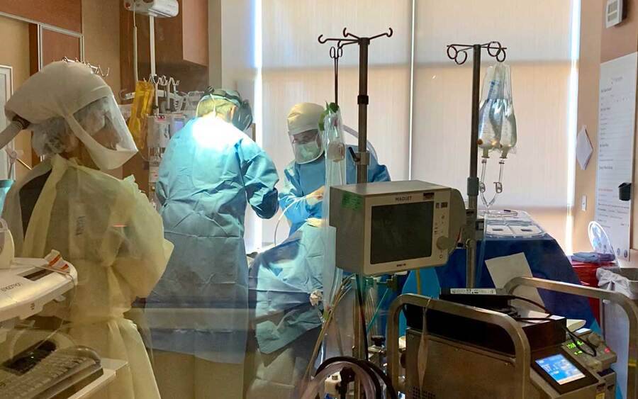 Three medical professionals in full PPE care for a patient with coronavirus in a hospital room at Scripps Health.