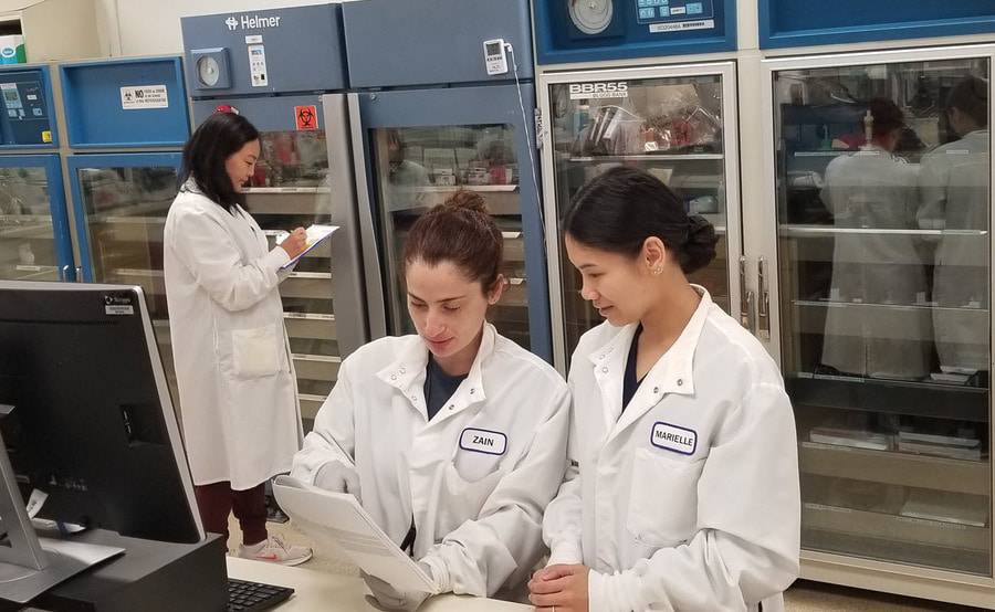 Two Scripps lab scientists in white coats review notes together.