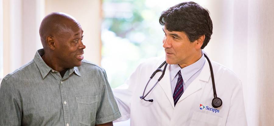 Dr. Gerard Lumkong talks with a man in a bright, sunny hallway, representing the expert, collaborative primary care at Scripps Coastal Medical Center.