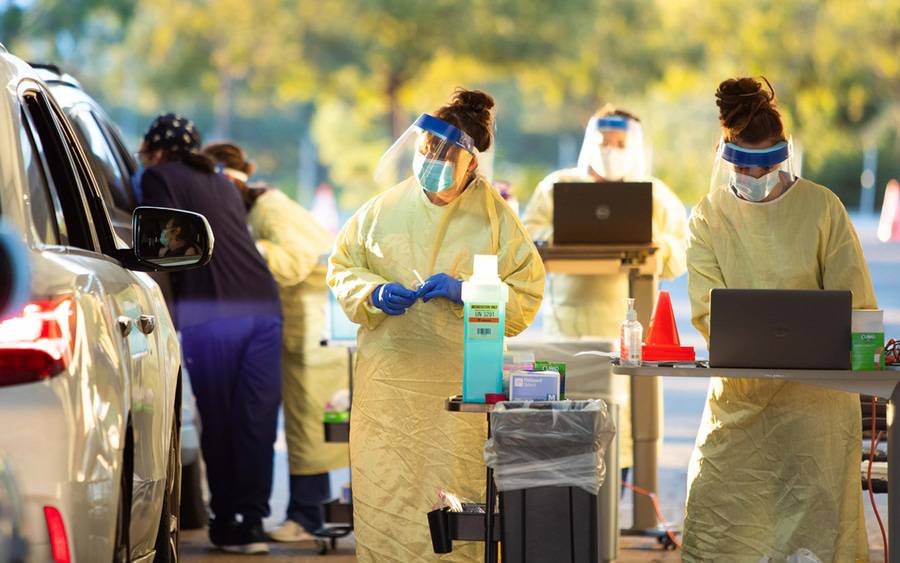 Scripps Health employees in masks and gowns while serving patients at a drive through COVID clinic early on in the pandemic.